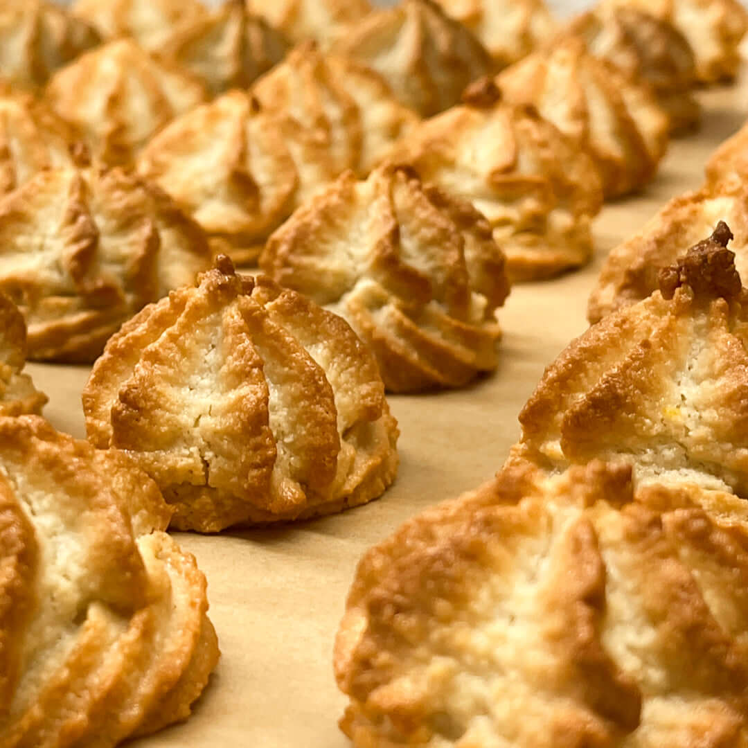 A close-up of rows of golden-brown True Delicious Italian Almond Cookies on parchment, highlighting their crisp, textured edges and toasted tops—gluten-free treats inspired by a classic Sicilian recipe.