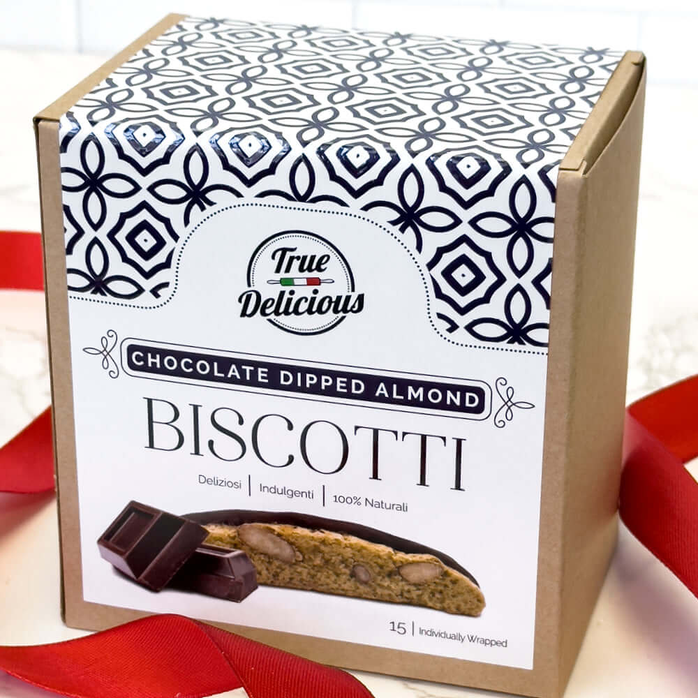 A box of True Delicious 2x Chocolate Dipped Almond Biscotti Individually Wrapped, featuring a decorative patterned label, an image of chocolate-dipped biscotti, and a partially visible red ribbon beside the box.