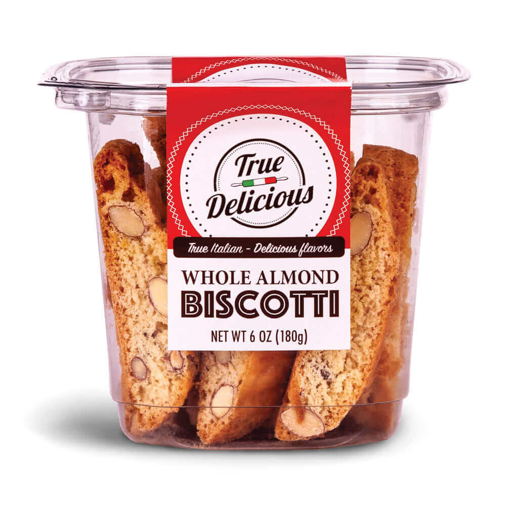 A clear plastic container labeled True Delicious Whole Almond Biscotti contains several cookies made with premium California almonds. The red and white label features Net wt 6 oz (180g) and highlights the authentic Tuscan recipe.