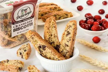 Cranberry biscotti with a package labeled 'True Delicious Cranberry Biscotti' on a white surface with cranberries.