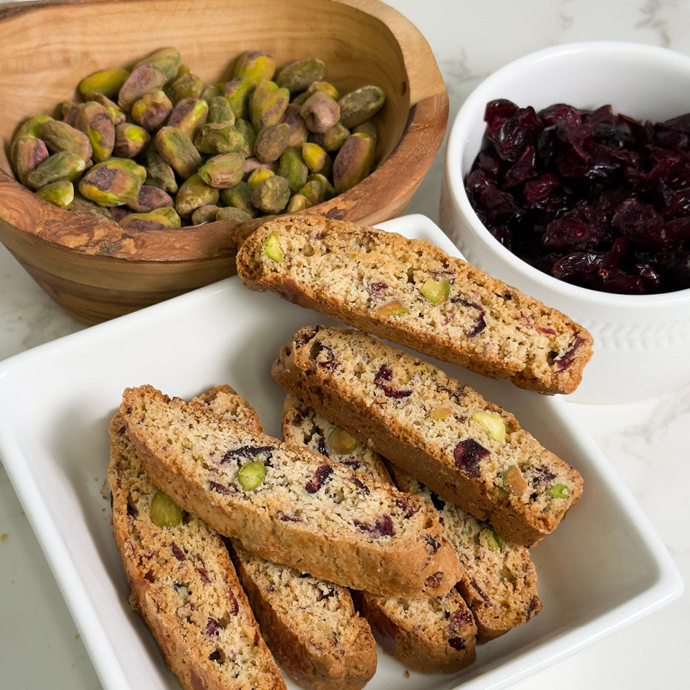 A bowl of pistachios and fresh fruit pair perfectly with True Delicious Cranberry Pistachio Biscotti - Limited Edition for a delightful snack.