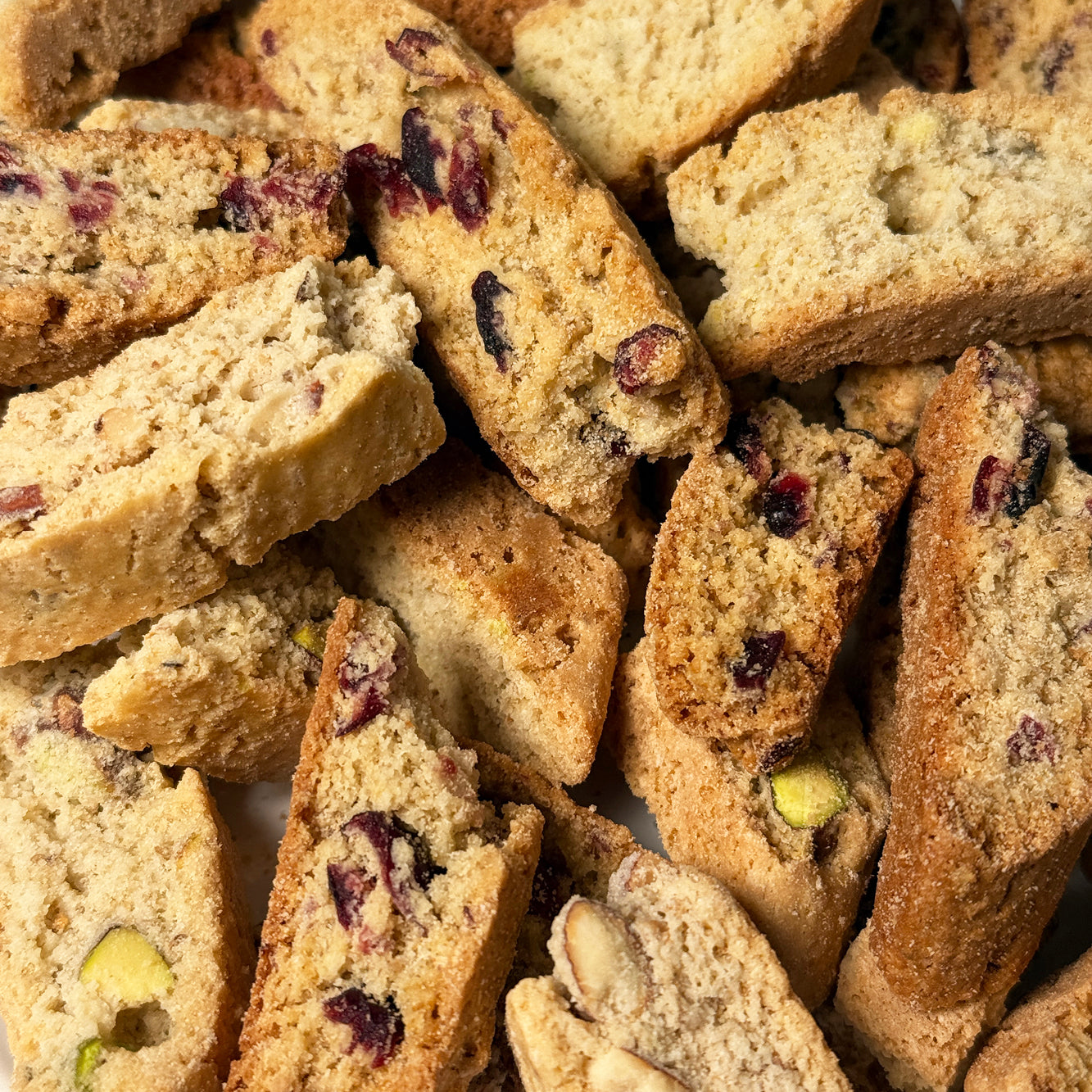 A close-up view of True Delicious Biscotti’s GF Ingredients Biscotti Bits - Mixed Flavors (2lbs) shows an enticing assortment of gluten free biscotti pieces, featuring visible bits of almond, cranberry, pistachio, and dried fruit throughout—all piled together with a handful of delicious biscotti ends on display.