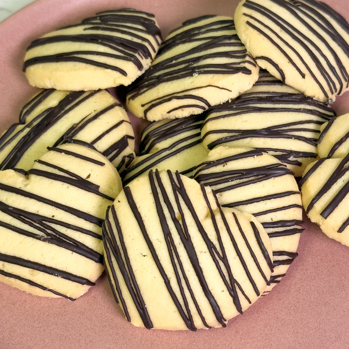 True Delicious Love Cookies feature heart-shaped shortbread and round cookies drizzled with dark chocolate, beautifully arranged on a light pink surface—perfect for sharing on Valentine’s Day.