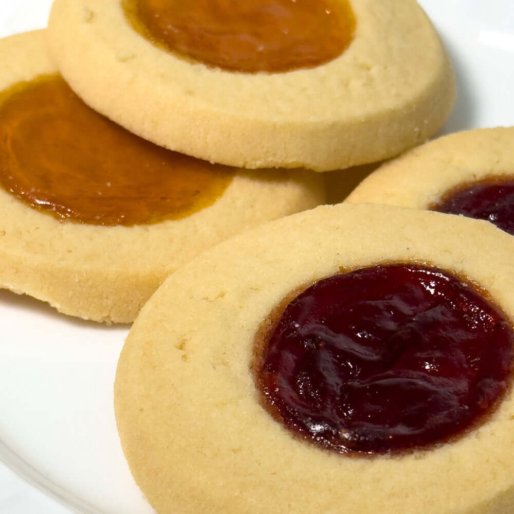 Close-up of True Delicious Jam Cookies Apricot Raspberry—three buttery cookies with apricot and raspberry jam centers—arranged on a white plate.