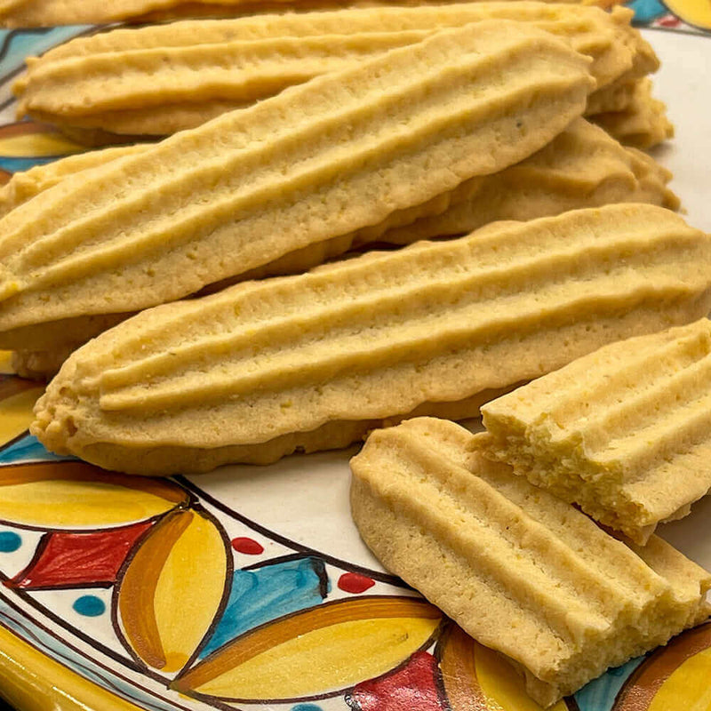 A decorative plate displays True Delicious Cookies Collection (10-Pack) Italian cookies, golden and ridged, with one broken to reveal its crumbly inside.